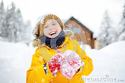 Happy preteen boy having fun playing with fresh snow during snowfall in european Alps. Child dressed in warm clothes, hat, hand Stock Photo