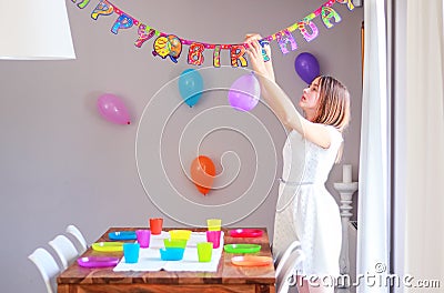 Happy preteen girl setting up table and hanging up balloons decorating house preparing to kids birthday party. Stock Photo