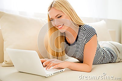 Happy pretty blonde typing on laptop while lying on couch Stock Photo