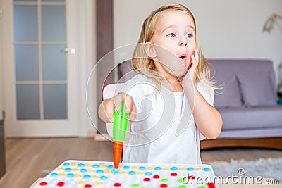 Happy pretty little blonde girl sitting at a table at home playing with a toy screwdriver and multicolor screws with Stock Photo