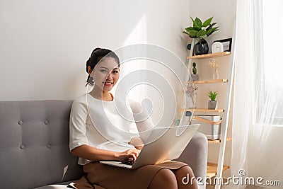 Happy pretty young woman sitting on sofa and using laptop at home Stock Photo