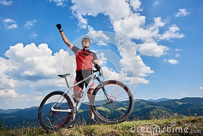 Happy professional sportsman cyclist standing with cross country bicycle on a hill, rasing hand Stock Photo