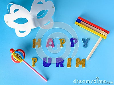 Happy Purim Jewish celebration holiday greeting card.White carnival mask,colorful wooden noisemakers on blue background. Stock Photo