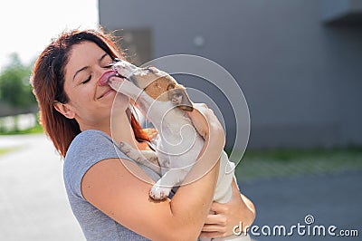 Happy red-haired woman hugs her little dog for a walk outdoors. Jack Russell Terrier licks the face of the female owner. Stock Photo