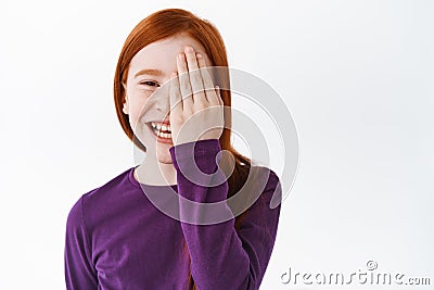 Happy redhead little girl, ginger kid hiding half of face behind hand and laughing, smiling cheerful, standing over Stock Photo