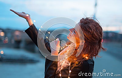 Happy redhead woman with fairy light garland at evening outdoors Stock Photo