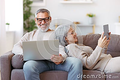 Happy relaxed old retired family couple using modern technologies laptop and digital tablet at home Stock Photo