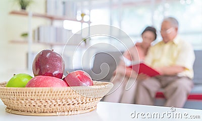 Happy retired couple reading book on a couch in living room with fresh fruit on the table to healthy eating and lifestyle Stock Photo