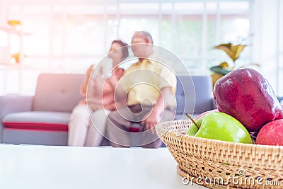 Retired asian couple reading book on a couch in living room with fresh fruit on the table to healthy eating and lifestyle Stock Photo