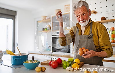 Happy retired senior man cooking in kitchen. Retirement, hobby people concept Stock Photo