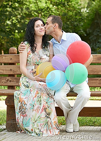 Happy romantic couple sit on bench in city park and kiss, summer season, adult people man and woman Stock Photo