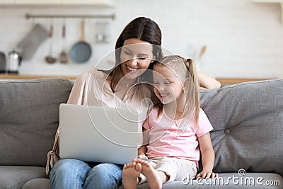 Happy 30s mommy watching funny cartoons with little daughter. Stock Photo