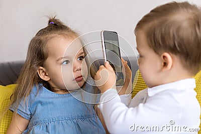 happy and sad little cute preschool siblings baby brother and child sister talk video conference on yellow gray sofa Stock Photo