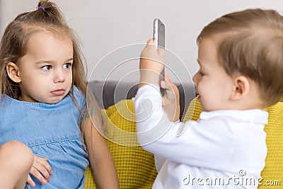 happy and sad little cute preschool siblings baby brother and child sister talk video conference on yellow gray sofa Stock Photo