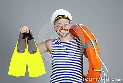 Happy sailor with ring buoy and swim fins on grey background Stock Photo