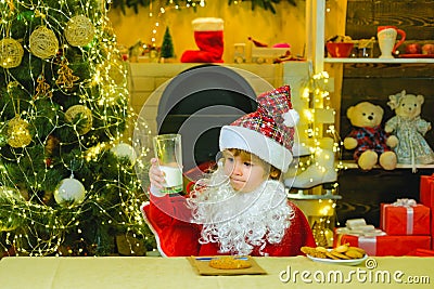 Happy Santa Claus helper with glass of milk and cookie. Little Santa picking cookie and glass of milk at home. Stock Photo