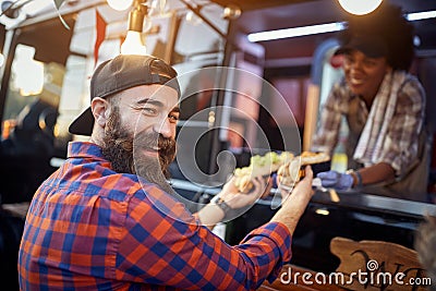 Happy, satisfied caucasian beardy male customer taking sandwiches from a polite employee in fast food service, looking at camera Stock Photo
