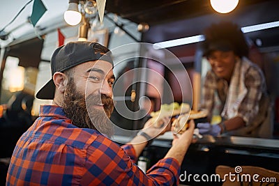 Happy, satisfied caucasian male with beard customer receiving sandwiches from a polite employee in fast food service, turning his Stock Photo