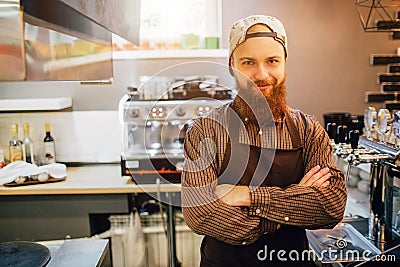 Happy and satisfied young man stand in kitchen and pose on camera. Barista wears crop. There are coffee machine and Stock Photo