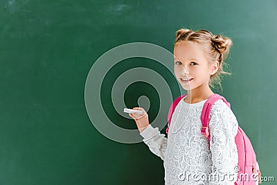 happy schoolchild holding chalk near chalkboard on green . Stock Photo