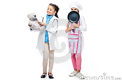 happy schoolchildren in costumes of doctor and chef holding teddy bear and frying pan Stock Photo