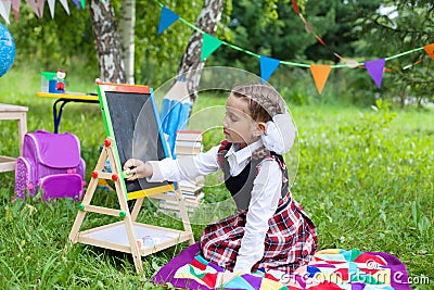 Happy schoolgirl child kid girl sitting on grass and writing on Stock Photo