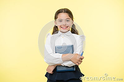 Happy schoolgirl hold book on yellow background. Little girl smile with textbook and pen. Confident in her knowledge Stock Photo