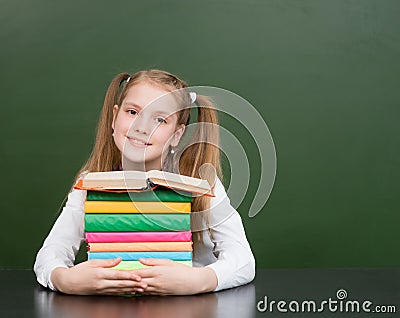 Happy schoolgirl with pile books near empty green chalkboard Stock Photo