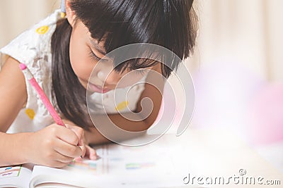 Happy schoolgirl works on her homework, write something in her n Stock Photo