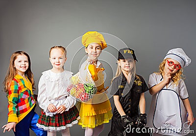 Happy schoolgirls in costumes of different professions isolated on grey background. Stock Photo