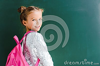 happy schoolkid smiling while standing with backpack on green . Stock Photo