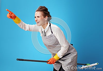Happy scrubwoman pointing at something using mop as broomstick Stock Photo