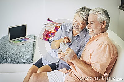 Happy senior adult couple of cacuasian people in love sitting at home on the sofa and taking a wood hand made hearth on hands. Stock Photo