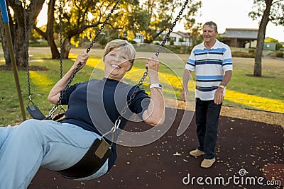 Happy senior American couple around 70 years old enjoying at swing park with husband pushing wife smiling and having fun Stock Photo