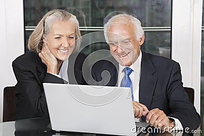 Happy senior business couple looking at laptop white sitting at table Stock Photo