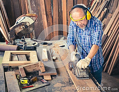 Happy senior carpenter using an electric planer Stock Photo