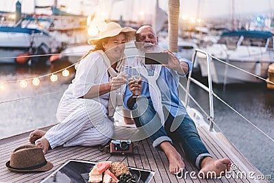 Happy senior couple doing selfie, cheering with champagne on a sailboat during anniversary vacation - Joyful elderly lifestyle, Stock Photo
