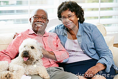 Happy Senior Couple Sitting On Sofa With Dog Stock Photo