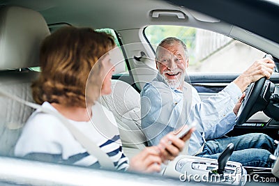 Happy senior couple with smartphone sitting in car, going on trip. Stock Photo