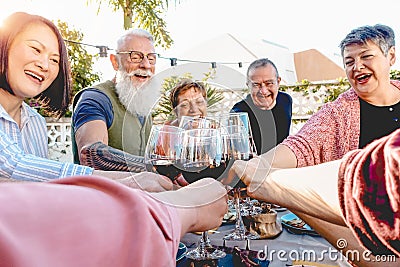 Happy senior friends toasting with red wine glasses at dinner on patio - Mature people having fun dining together outside Stock Photo