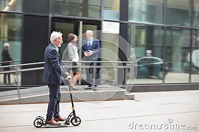 Happy senior businessman commuting to work on a kick scooter Stock Photo