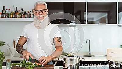 Happy senior man having fun cooking at home - Elderly person preparing health lunch in modern kitchen Stock Photo