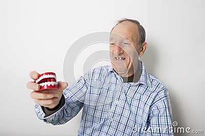 Happy senior man holding dentures against gray background Stock Photo