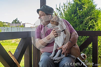 Senior man taking his lovely basenji dog and watching both while sitting on summer veranda Stock Photo