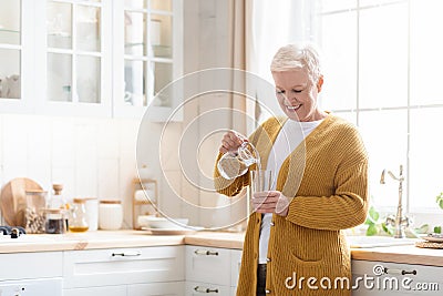 Happy senior woman pouring water into glass in kitchen Stock Photo