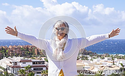 Happy senior woman enjoying sea holiday in winter. Positive, optimistic active retiree smiling with raised arms Stock Photo
