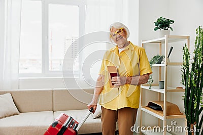 Happy senior woman with passport and travel ticket packed a red suitcase, vacation and health care. Stock Photo