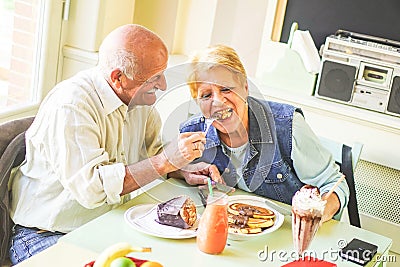 Happy seniors couple eating pancakes in a bar restaurant - Retired people having fun enjoying lunch together Stock Photo