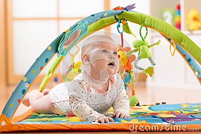 Happy seven months baby girl plays lying on colorful playmat Stock Photo