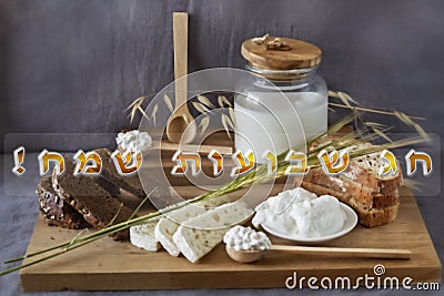 Happy Shavuot - Hebrew inscription in the photo with traditional products for the Jewish holiday Shavuot. Postcard on Shavuot Stock Photo